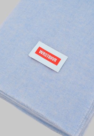 Bufanda de lana azul claro doblada con una etiqueta rectangular blanca con la inscripción "WRSTBHVR" en letras rojas y negrita.