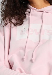 Felpa rosa chiaro realizzata in tessuto morbido; presenta una stampa del logo bianco, cappucci regolabili e polsini a coste.