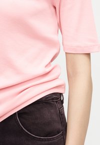 Άτομο που φοράει ανοιχτό ροζ κοντομάνικο πουκάμισο, καλά μέσα σε μαύρο τζιν ψηλόμεσο με εμφανείς ραφές και μπροστινή τσέπη.