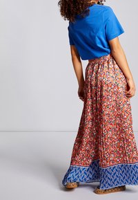 Camisa azul de manga corta combinada con una larga falda maxi estampada con diseños florales en rojo y verde, terminando con un dobladillo en forma de chevron azul.