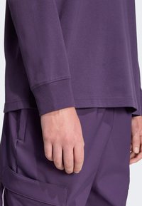Purple long-sleeve shirt with a round neckline, made of soft fabric, featuring ribbed cuffs, paired with matching pants.