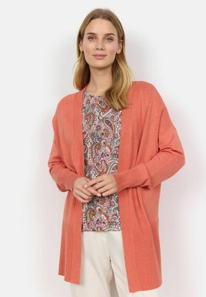 Svijetloružičasti kardigan izrađen od mekanog materijala, s otvorenim prednjim dijelom, rebrastim manžetama i opuštenim krojem. Uparen s košuljom u više boja s paisley uzorkom.