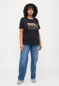 Svart t-skjorte med et gull leoparddesign og tekst. Kombinert med lyseblå straight-leg jeans og sølv sneakers. Avslappet passform.