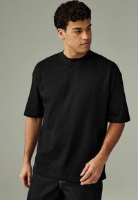 Sort T-shirt med kortærmer og rund halsudskæring, i afslappet pasform, lavet af blødt bomuldsstof, parret med mørke denim jeans.