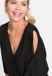 Haut noir avec un décolleté en V profond et des manches courtes, présentant des accents découpés. Fabriqué en tissu doux, conçu avec une coupe décontractée.