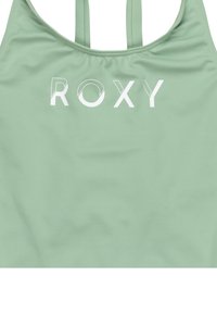 Groene sportbeha van gladde stof met dunne bandjes en een witte "ROXY" logo over de borst.