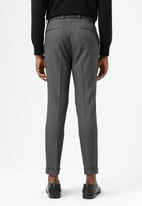 Graue, maßgeschneiderte Hose mit schlanker Passform, ausgestattet mit Gesäßtaschen, einem Umschlag am Saum und einer glatten Textur. Getragen mit schwarzen Schuhen.