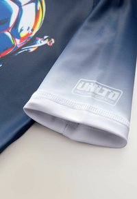 Kortärmad sporttröja i marinblått och gradientljusblått, tillverkad av ett mjukt material med logotryck och en livfull bollgrafikdesign.