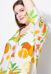 Hvid kortærmet top med et levende citrus- og blomstermønster i orange, gul, pink og grøn. V-hals design og afslappet pasform.