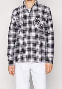Zwart-wit geruit overhemd met lange mouwen, knoopsluiting aan de voorkant en een borstzak aan de linkerkant. Gemaakt van een lichtgewicht stof met een gladde textuur.
