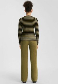 Haut à manches longues noir et olive à rayures associé à un pantalon large en olive à côtes. Les tissus sont ajustés et texturés.