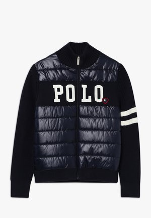 Veste zippée bleu marine avec un devant matelassé, arborant un grand texte blanc "POLO", un col côtelé et des manches en maille texturée avec des rayures blanches.