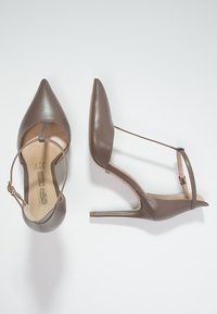 Chaussures à talons hauts en cuir marron avec un bout pointu, une sangle de cheville et un design épuré. Présente une texture lisse et une semelle de couleur claire.