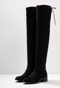 Schwarze Wildlederstiefel über das Knie mit flachem Absatz, runder Spitze und einem Schnürdetail an der Oberseite. Verfügt über einen seitlichen Reißverschluss für ein einfaches Anziehen.
