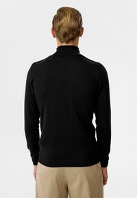 Zwarte coltrui met een gladde textuur, lange mouwen en een aangesloten ontwerp. Ribgebreide manchetten en zoom voegen structuur toe.