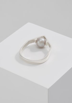 Silberner Ring mit einer großen runden Perle, gesetzt in ein offenes, unregelmäßiges geometrisches Band auf einem weißen Sockel.