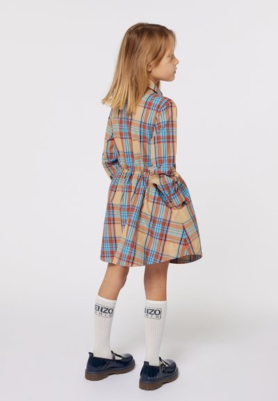 Abito a maniche corte a scacchi nei colori beige, rosso e blu; presenta una cintura, una gonna svasata ed è abbinato a calze bianche e scarpe nere.