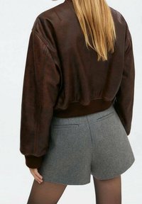 Hnědá kožená bombardovací bunda s ribbovaným lemem, doplněná šedými vlněnými šortkami. Má uvolněný střih a bezšvové detaily na zadní straně.
