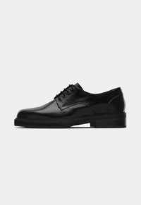 Chaussure noire en cuir à lacets avec une finition lisse, bout arrondi, profil bas et semelle épaisse en caoutchouc. Design minimaliste avec des coutures discrètes.