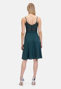 Turkusowa sukienka koktajlowa z dopasowaną, koronkową górą i zwiewnym dołem, z regulowanymi ramiączkami i ukrytym zapięciem z tyłu.