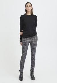 Schwarzes Langarmshirt aus strukturiertem Stoff, figurbetontem Design und mit Knopfdetails. Gemusterte, figurbetonte Hose mit einem geometrischen Muster in Marineblau und Creme.