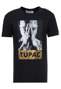 T-shirt nera in cotone, con una grafica frontale di una persona con le mani giunte e la parola "TUPAC" in caratteri dorati in grassetto sottostante.