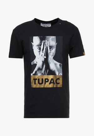 Zwarte t-shirt gemaakt van katoen, met een vooraanstaande afbeelding van een persoon met samengevouwen handen en het woord "TUPAC" in vetgouden letters eronder.