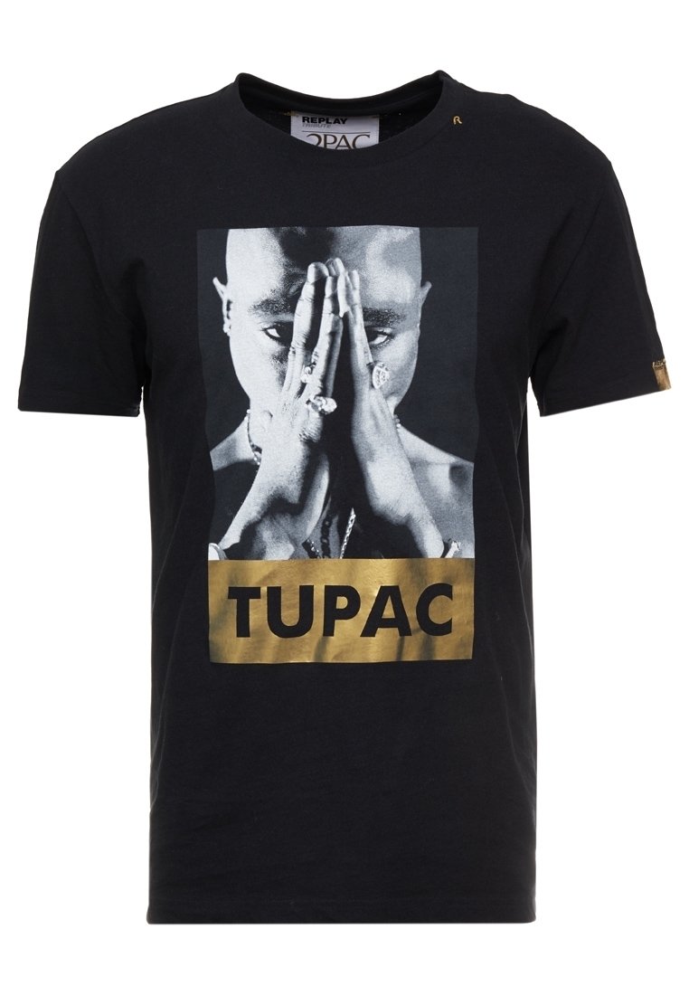 T-shirt nera in cotone, con una grafica frontale di una persona con le mani giunte e la parola "TUPAC" in caratteri dorati in grassetto sottostante.