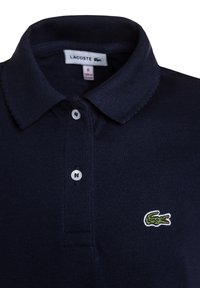 Polo bleu marine Lacoste avec col, deux boutons blancs et petit logo crocodile vert sur la poitrine.