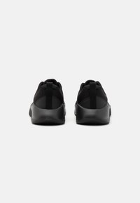 Un par de zapatillas deportivas negras vistas desde atrás, con parte superior de malla, lengüetas y suelas de goma gruesas sobre un fondo blanco.
