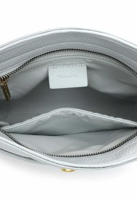 Wnętrze białej skórzanej torebki z zasuwaną przegrodą i gładką podszewką. Zawiera małą metkę z nazwą marki „Tamaris.”