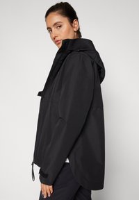 Czarna wodoodporna kurtka z kapturem, zapinana na zamek, z regulowanymi mankietami i luźnym krojem. Gładka faktura i minimalistyczny design.