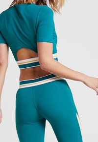 Teal träningslinne med korta ärmar, med en skärning på baksidan. Matchat med högmidjade teal leggings, accentuerade med horisontella randiga band.