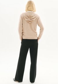Sudadera de punto beige con una textura suave y una capucha grande y caída. Combinada con pantalones de pierna ancha negros de cintura alta.