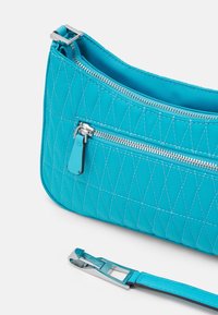 Borsa a tracolla turchese trapuntata con finiture in argento. Presenta una chiusura con zip e una tasca esterna con zip. Inclusa una tracolla regolabile.