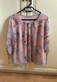 Blusa de tela ligera en color rosa claro con estampado floral, de medias mangas y cuello redondeado. Presenta pliegues y lazos ajustables en las mangas.