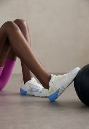 Weiße Sportschuhe haben ein Mesh-Design mit grünen Akzenten und einer blauen Sohle, die ein strukturiertes Muster an der Seite hervorhebt.