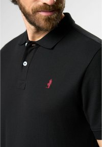 Black polo shirt featuring a textured design, three-button placket, and a small red embroidered logo on the left chest.