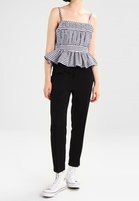 Pruhovaný peplum top s přiléhavým živůtkem, elastickým pasem a tenkými ramínky, spárovaný s černými úzkými kalhotami a bílými vysokými teniskami.