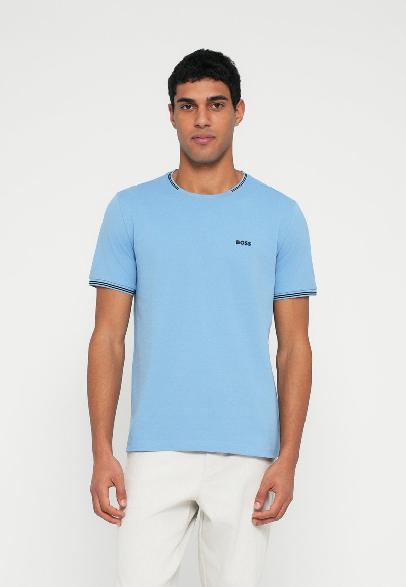 Jasnoniebieska koszulka wykonana z miękkiego materiału, z okrągłym dekoltem wykończonym kontrastową czarno-białą lamówką oraz małym czarnym logo "BOSS" na piersi.