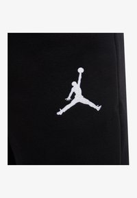 Schwarzer Sweatshirtstoff mit einem weißen, eingestickten Jumpman-Logo. Das Design ist schlicht und sportlich und hebt das Logo deutlich hervor.