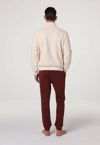 Pullover in pile crema con collo alto, vestibilità comoda, polsini a costine, abbinato a pantaloni jogger bordeaux scuro con vita e polsini elasticizzati.