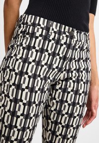 Pantalones de patrón negro y crema con un diseño geométrico, textura de denim, bolsillos delanteros y un cierre de botón metálico.