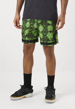 Grønne slangeprint shorts med sort kant, lavet af et let stof og med en afslappet pasform, parret med sorte sportssokker og sko.