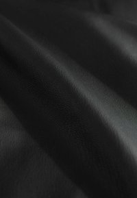 Nahaufnahme eines schwarzen strukturierten Stoffes mit subtilen Wellen und detaillierten Maserungen.