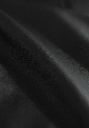 Tekstureeritud must nahk pehme, matt viimistlusega, mis näitab musta erinevaid varjundeid voltide ja kortsude kohal.