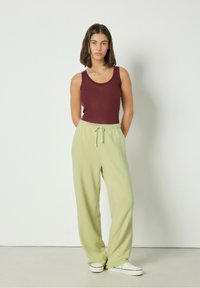 Burgundska majica bez rukava kombinirana s svijetlozelenim, širokim hlačama s elastičnim pojasom i vezicom. Bijeli tenisice upotpunjuju odjevnu kombinaciju.