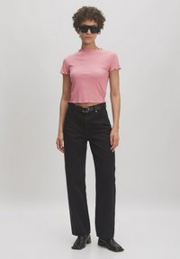 Roze cropped t-shirt met gerimpelde zoom, gecombineerd met zwarte high-waisted broek en zwarte hakken. Model draagt oversized zwarte zonnebril.