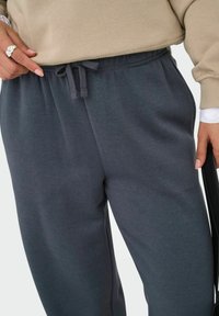 Mørkegrå sweatpants med elastisk talje og snøre, lavet af blødt materiale. Sidelommer og en afslappet pasform er synlige.