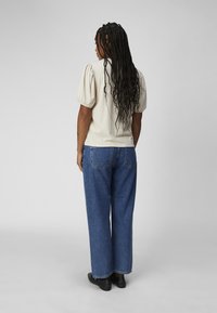 Creme, ribbet top med puffede ærmer, parret med højtaljede, loose blå denimjeans og sorte ankelstøvler.